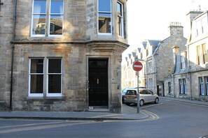 A stone building with a black door and windows, a no entry sign, and a parked car on a street.
