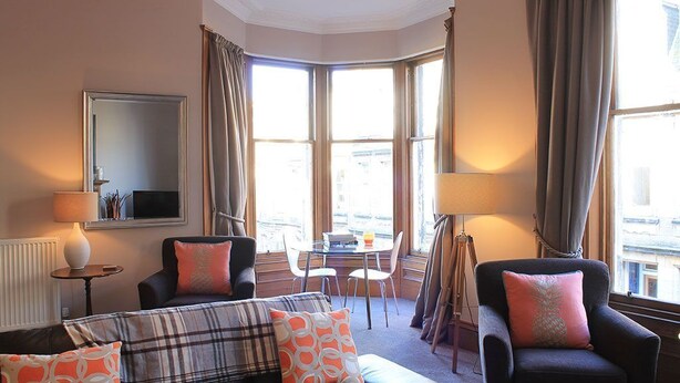 A hotel room with a large bay window, a sofa, two armchairs, a small table, and a floor lamp. - 10 Murray Park  375840 (St. Andrews)