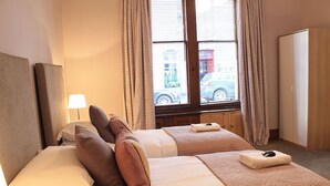 A hotel room with two beds, a window with curtains, a lamp, and a wardrobe. - 10 Murray Park  375840 (St. Andrews)