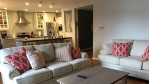A modern living room with a grey sofa set, a coffee table, and a kitchen in the background. - TO Stays - Waterfront Lake House Retreat (Ryerson)