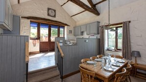 A rustic kitchen with wooden beams, a dining table set for six, and a view of the outside. - Mill Barn (Hot Tub) 2 bedrooms (Brampton)