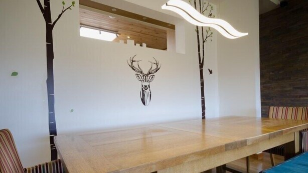 A long wooden dining table with striped chairs, a wall-mounted light fixture, and a tree decal with a deer head. - Kirkstone Lodge 72673 (Kingussie)