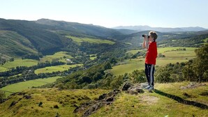 A person standing on a grassy hill overlooking a valley with rolling hills and a river. - Achmony Green lodge (Inverness)