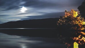 A castle on a hill overlooking a calm body of water, with a moonlit sky. - Achmony Green lodge (Inverness)
