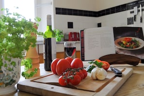 A kitchen counter with fresh tomatoes, a bottle of wine, a cutting board, and a cookbook. - The South Wing (Oban)