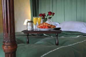 A neatly arranged breakfast tray with croissants, strawberries, a pitcher of roses, and two glasses of orange juice on a bed with green bedding and a wooden headboard. - The South Wing (Oban)