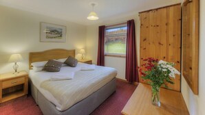 A bedroom with a bed, two bedside tables with lamps, a window with curtains, a wooden wardrobe, and a framed picture on the wall. - Poplar lodge (Oban)