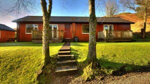 A wooden cabin with a front porch, a wooden deck, and a stone staircase leading to the door. - Poplar lodge (Oban)