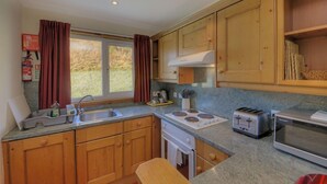 A compact kitchen with wooden cabinets, a gas stove, a toaster, and a sink. - Poplar lodge (Oban)