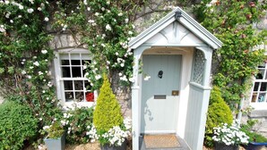 A small, light blue wooden structure with a door, surrounded by white flowers and greenery. - The Store House (Llandudno Junction)