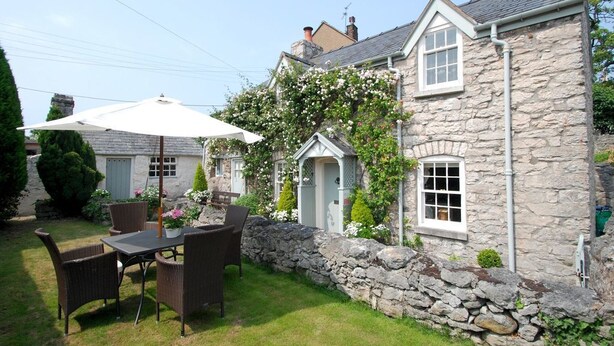 A stone house with a garden patio featuring wicker furniture and a white umbrella. - The Store House (Llandudno Junction)