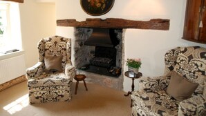 A cozy living room with a stone fireplace, two patterned armchairs, a small side table, and a wooden cabinet. - The Store House (Llandudno Junction)