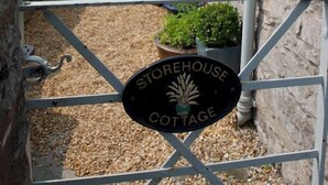 A stone cottage with a gravel pathway leading to a gated entrance. - The Store House (Llandudno Junction)