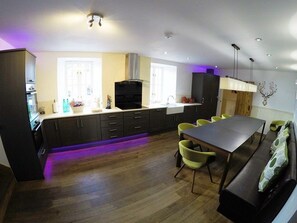 A modern kitchen with dark cabinets, a central island, and a dining area with a table and chairs. - Hillview Lodge 14669 (Ballindalloch)