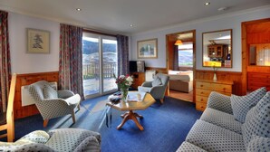 A hotel room with a large window, two armchairs, a sofa, a wooden cabinet, and a small table with a vase of flowers.
