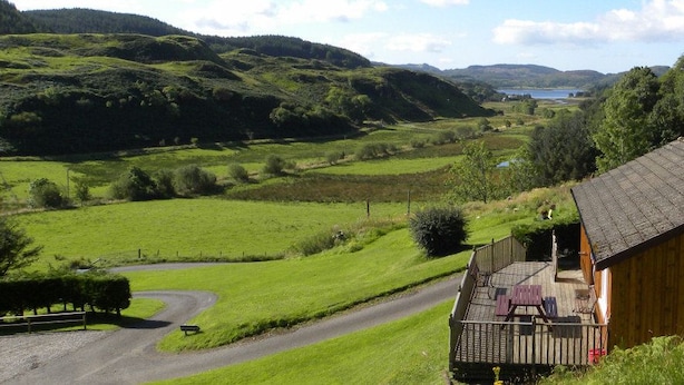 A wooden cabin with a porch, surrounded by lush green fields and hills.