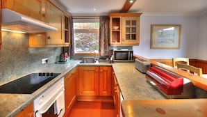 A compact kitchen with wooden cabinets, a built-in microwave, and a red bench.