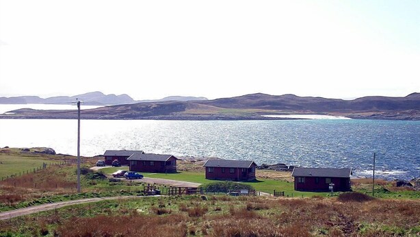 Zona costera con tres cabañas, una carretera y una masa de agua.