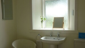 A bathroom with a white sink, a mirror, a window with frosted glass, and a chair.