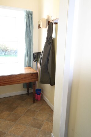 A room with a wooden table, a blue curtain, a hat, a jacket, and a blue bucket on the floor.