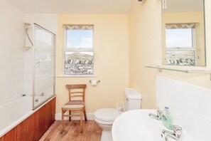 A bathroom with a bathtub, toilet, and sink. There is a window with a view of a stone wall and a chair.