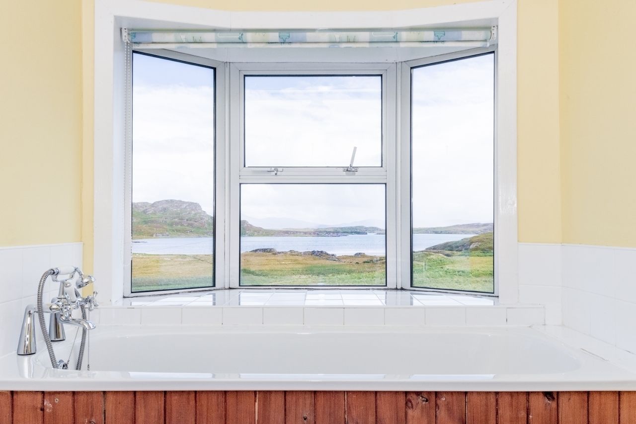 A bathroom with a large window offering a view of a coastal landscape.