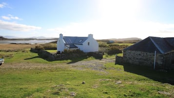 Una casa blanca con techo inclinado y paneles solares, rodeada de un campo cubierto de césped y un muro de piedra.