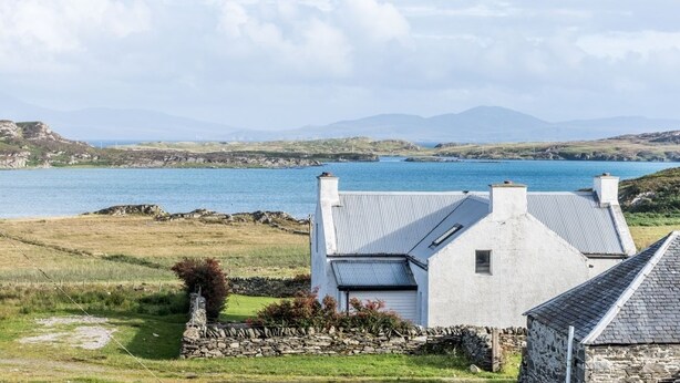 A coastal house with a stone foundation and white walls, overlooking a calm sea and distant mountains. - Garvard (Isle of Colonsay)