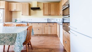 A kitchen with wooden cabinets, a table with chairs, and a refrigerator. - Garvard (Isle of Colonsay)