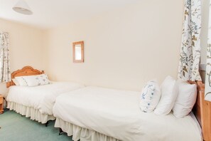 A bedroom with two single beds, a wooden headboard, a small mirror, and floral curtains.