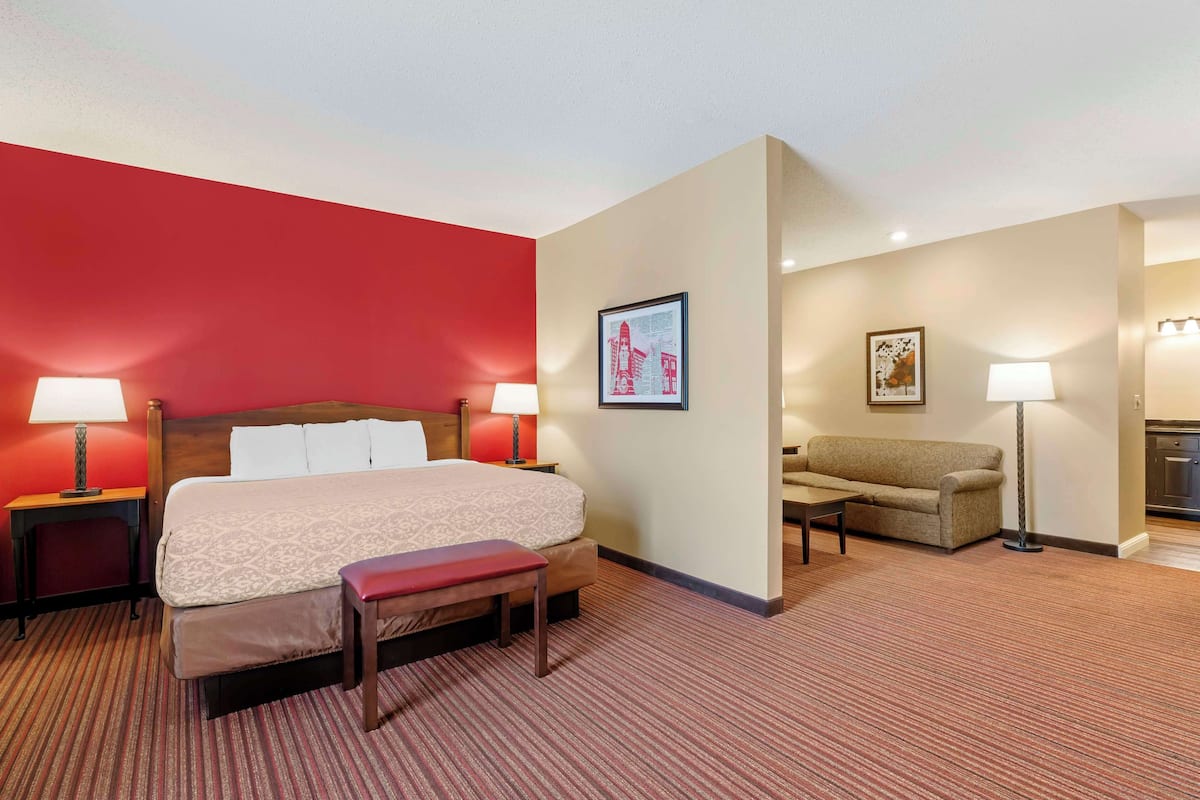 A hotel room with a large bed, two bedside tables with lamps, a bench, a sofa, and a small table.