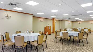 Un salón de conferencias con mesas y sillas redondas, un atril y suelo alfombrado.