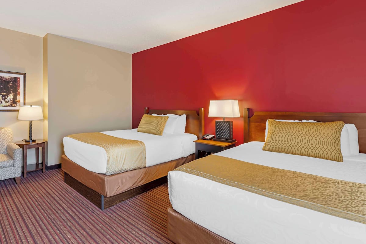 A hotel room with two beds, a desk, a chair, and a lamp.