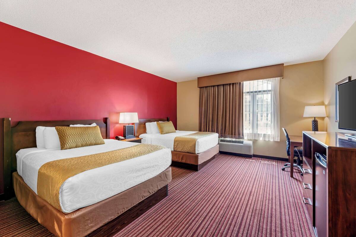 A hotel room with two beds, a desk, a television, and a window with curtains.
