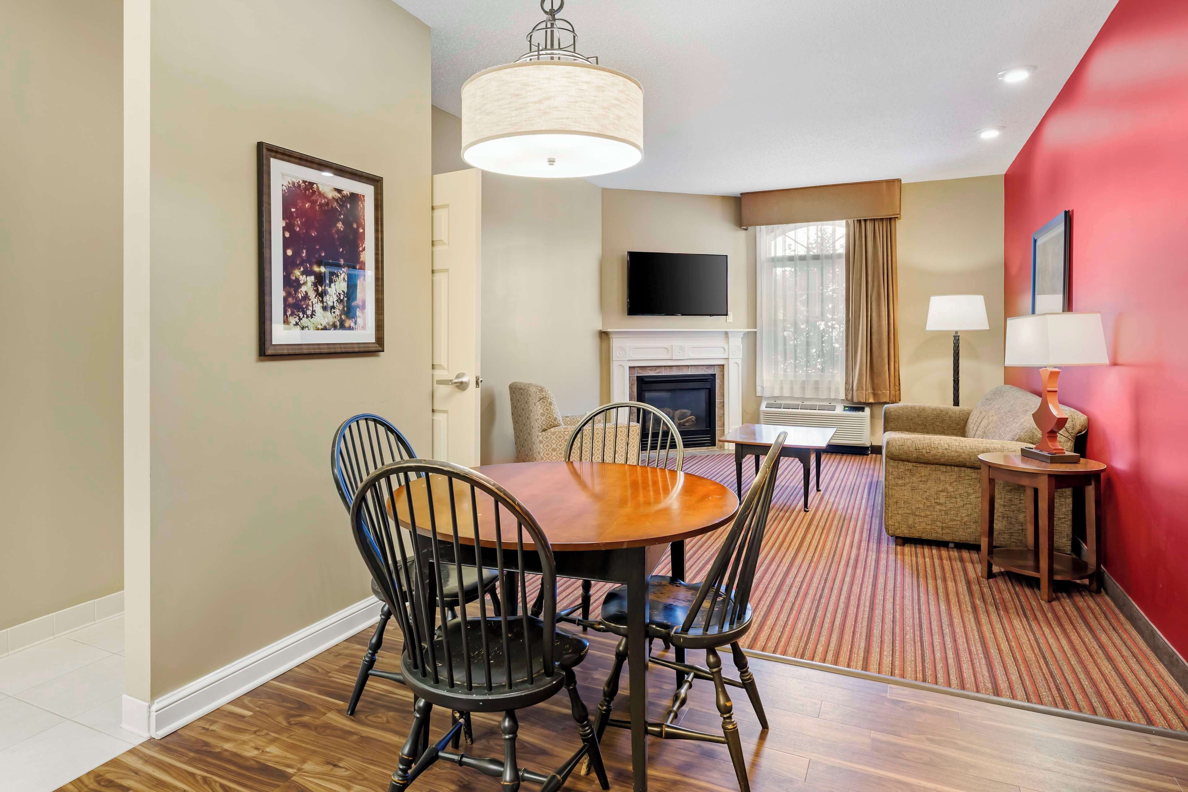 A dining area with a round table and chairs, a fireplace, a television, and a red accent wall.