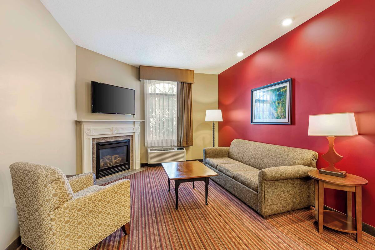 A hotel room with a fireplace, a television, a sofa, a coffee table, and a red accent wall.