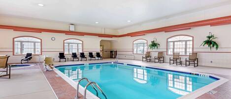 An indoor swimming pool with multiple lanes, chairs around the pool, and potted plants.