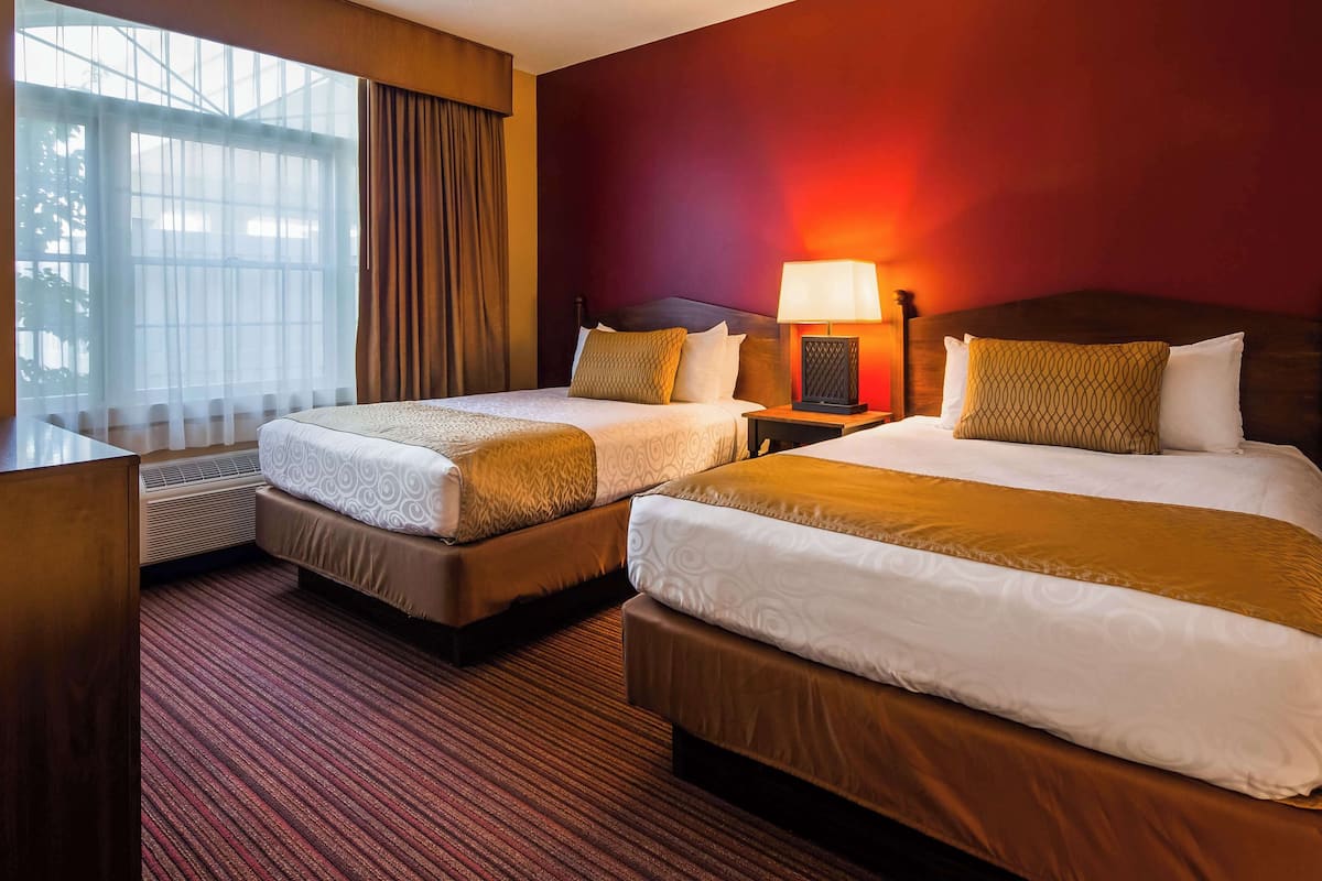 A hotel room with two beds, a desk, and a window with curtains.