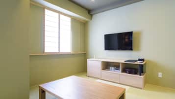Una habitación con una mesa de madera, un televisor montado en la pared, una ventana con persianas y un piso de color claro.