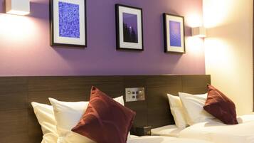 A hotel room with two beds, each with white bedding and red pillows, a wooden headboard, and three framed pictures on the wall.