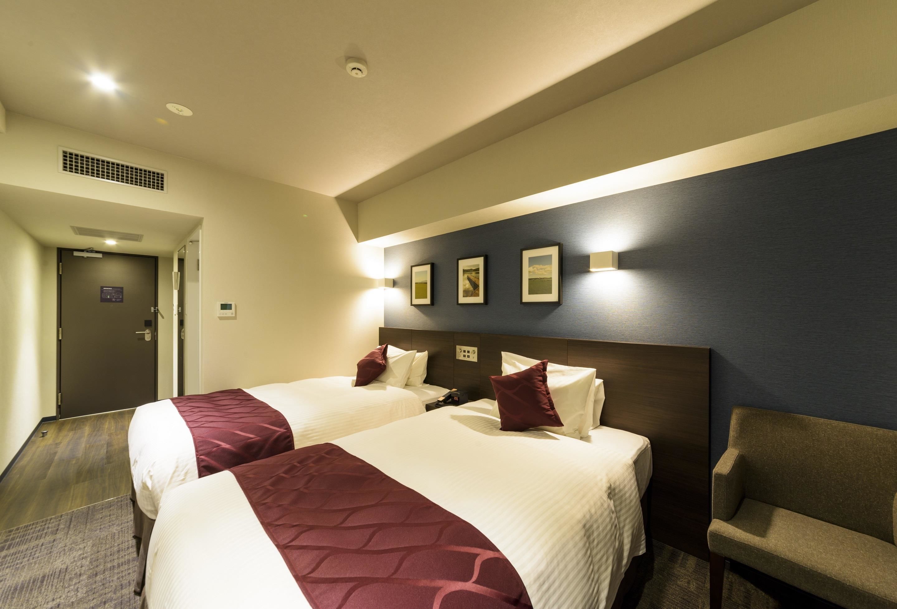 Habitación de hotel con dos camas, un sofá y un televisor instalado en la pared.