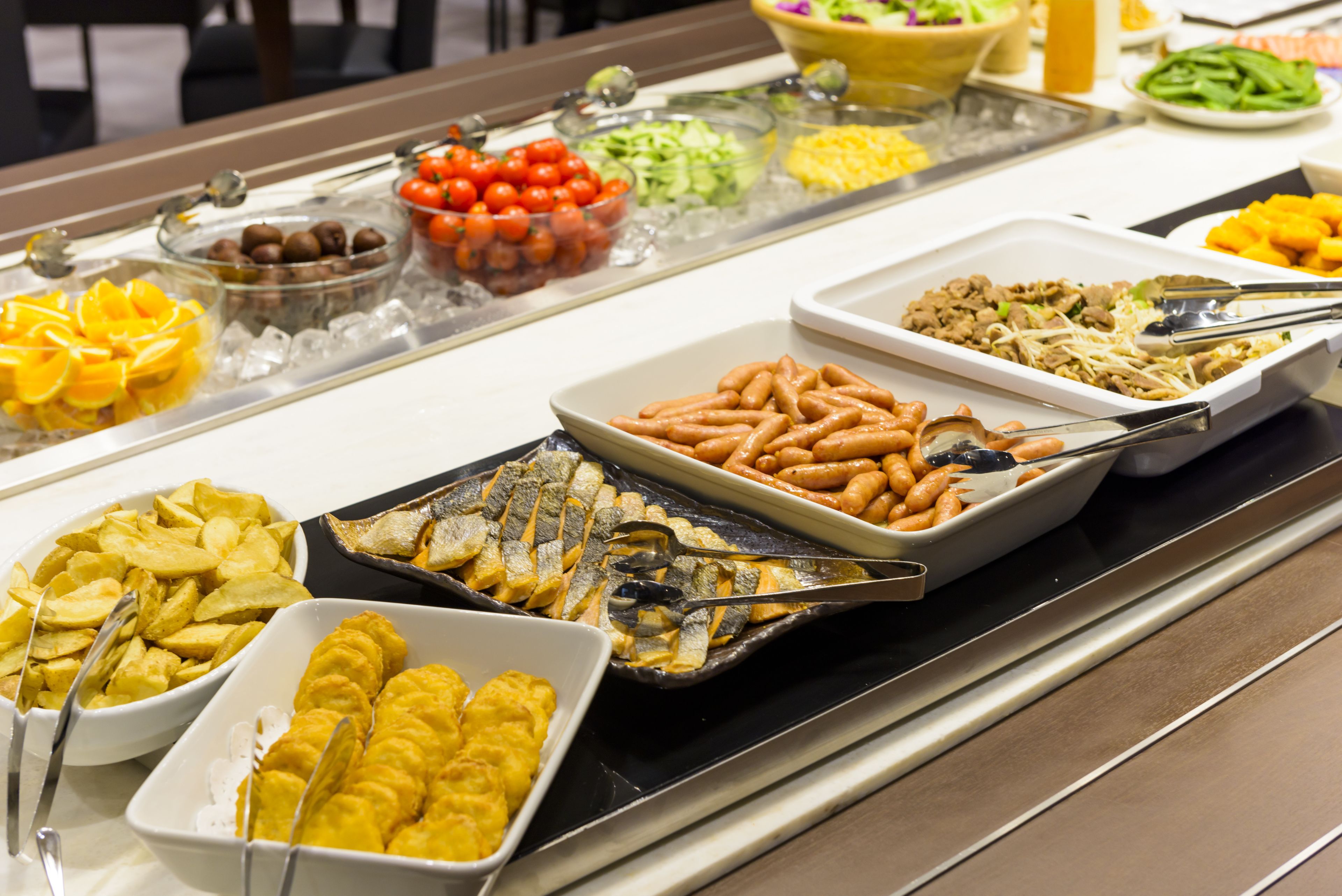 Un bufé con diversos alimentos, entre ellos frutas, verduras y platos cocinados.
