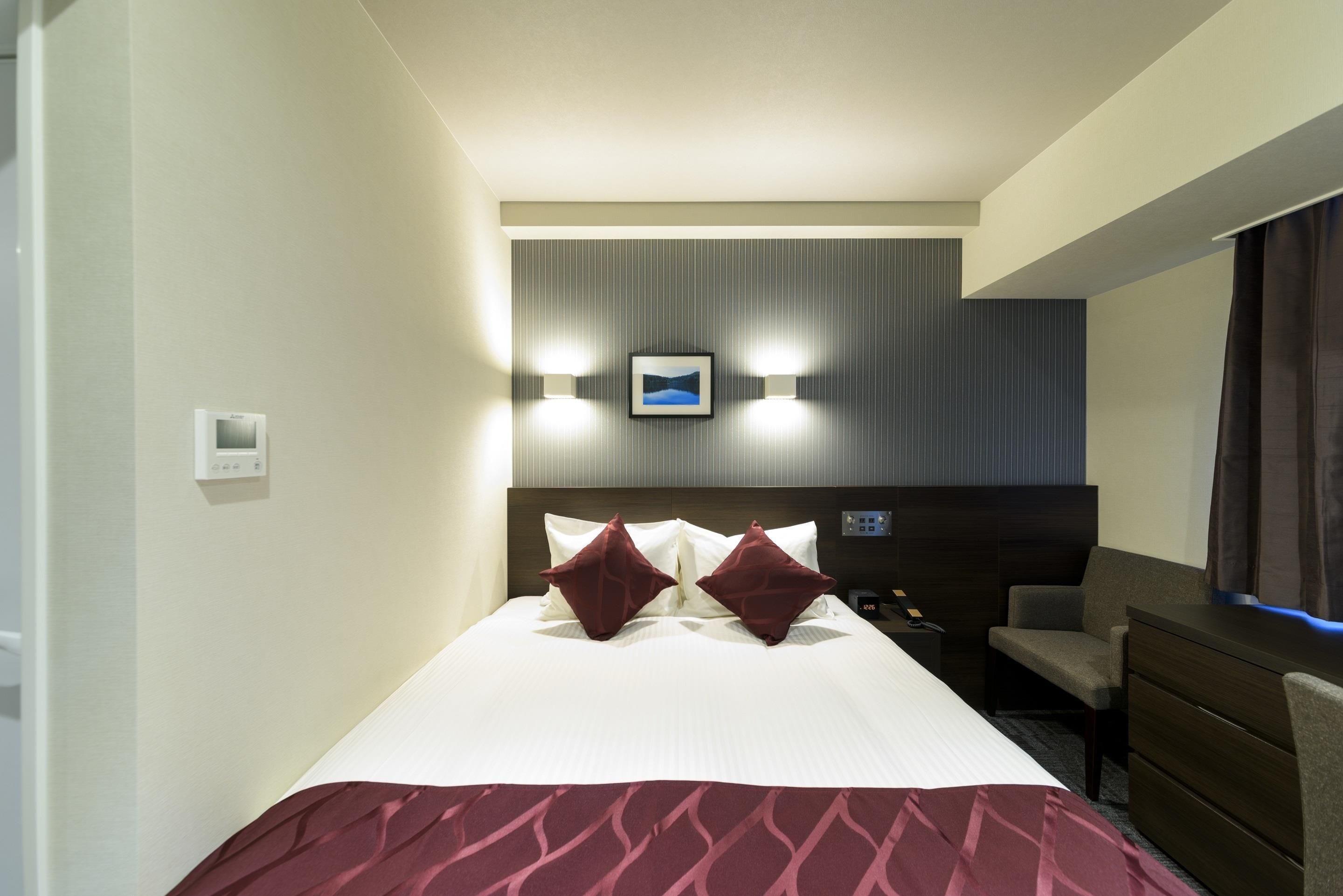 A hotel room with a bed, two wall-mounted lights, a nightstand, a chair, and a dresser.
