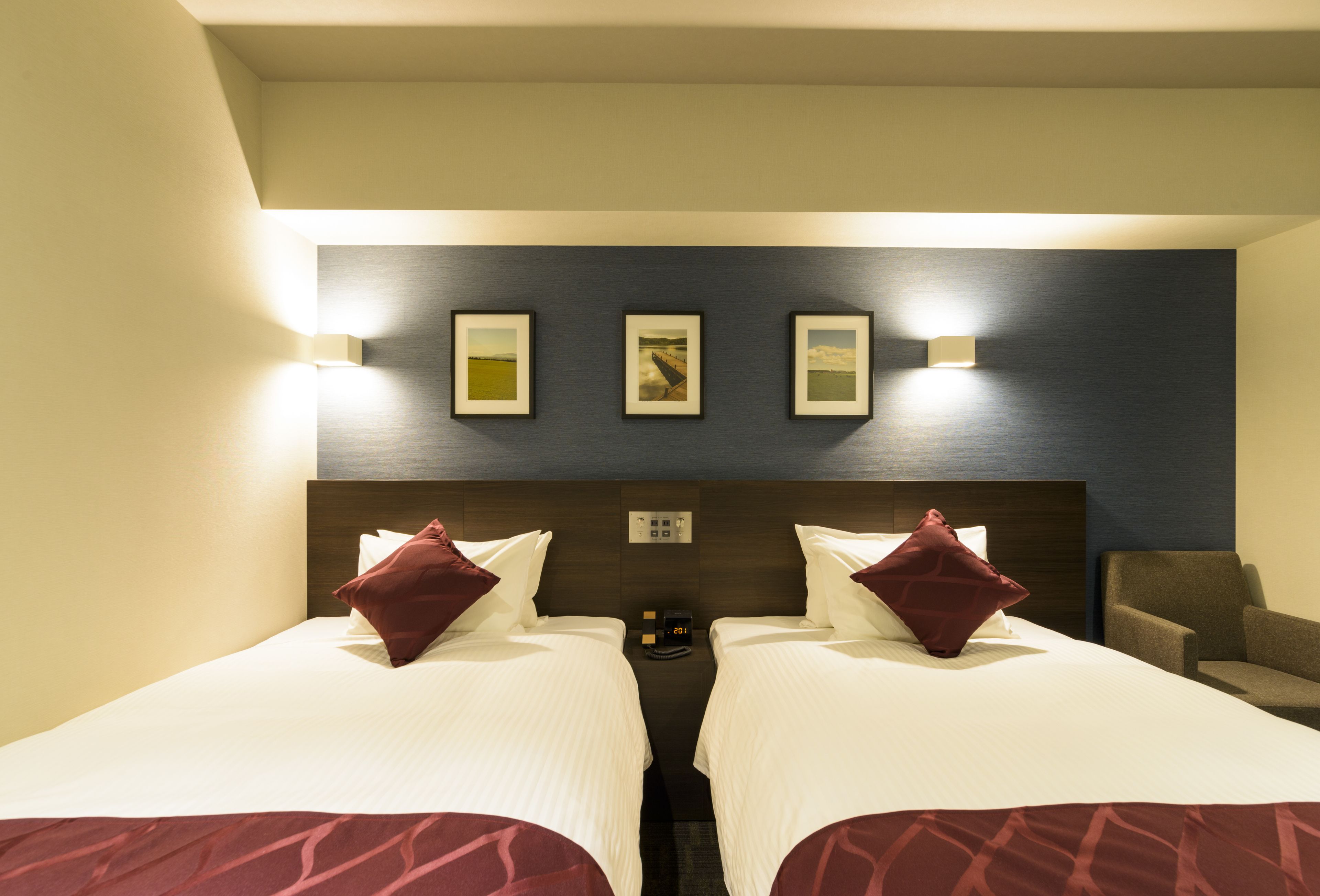 A hotel room with two beds, a nightstand, a clock, and wall-mounted lights.