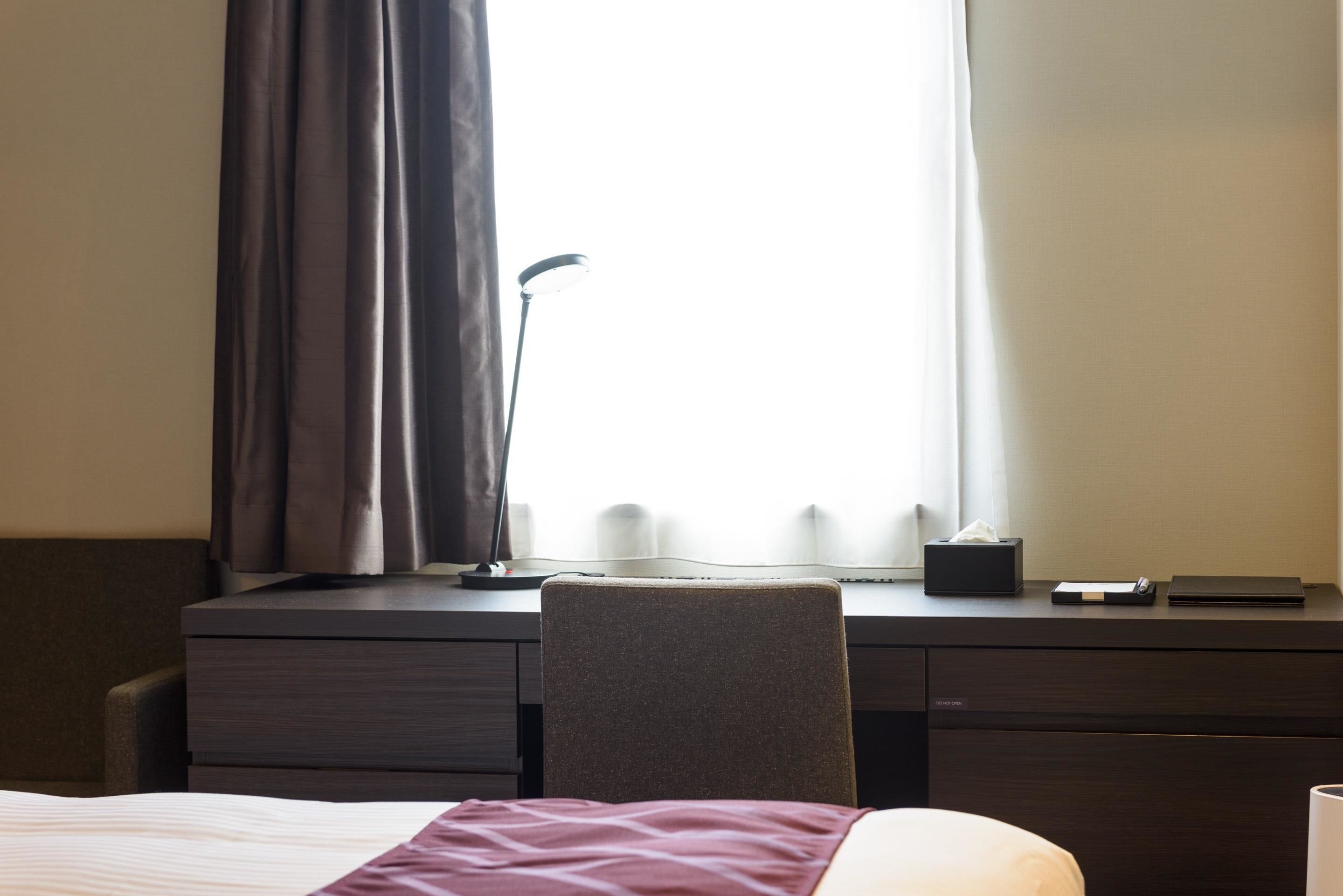 Una camera d'albergo con un letto, una scrivania con un computer, una sedia e una finestra con tende.