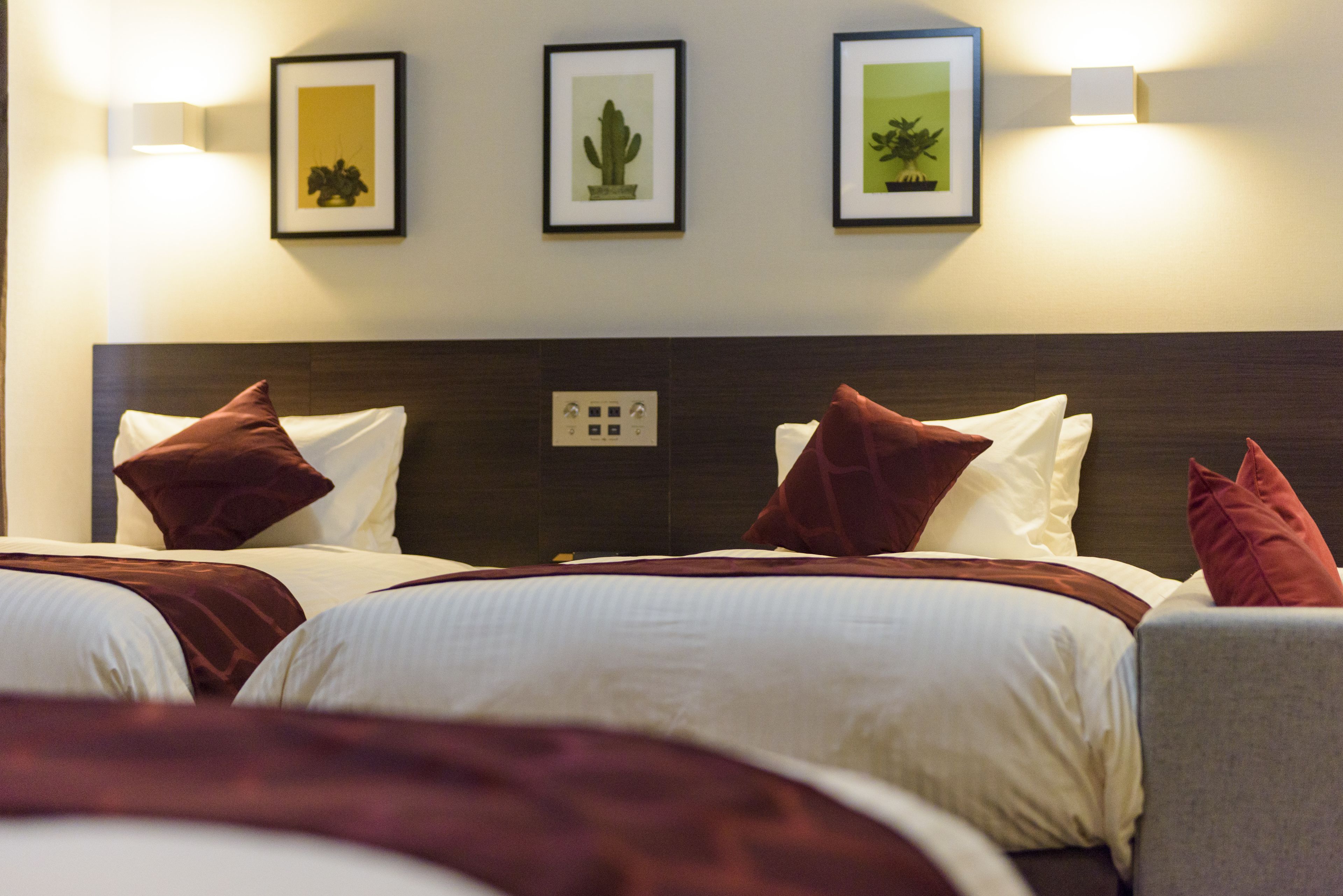 Habitación de hotel con dos camas, cada una con ropa blanca y almohadas marrones. Hay cuadros enmarcados en la pared sobre las camas.