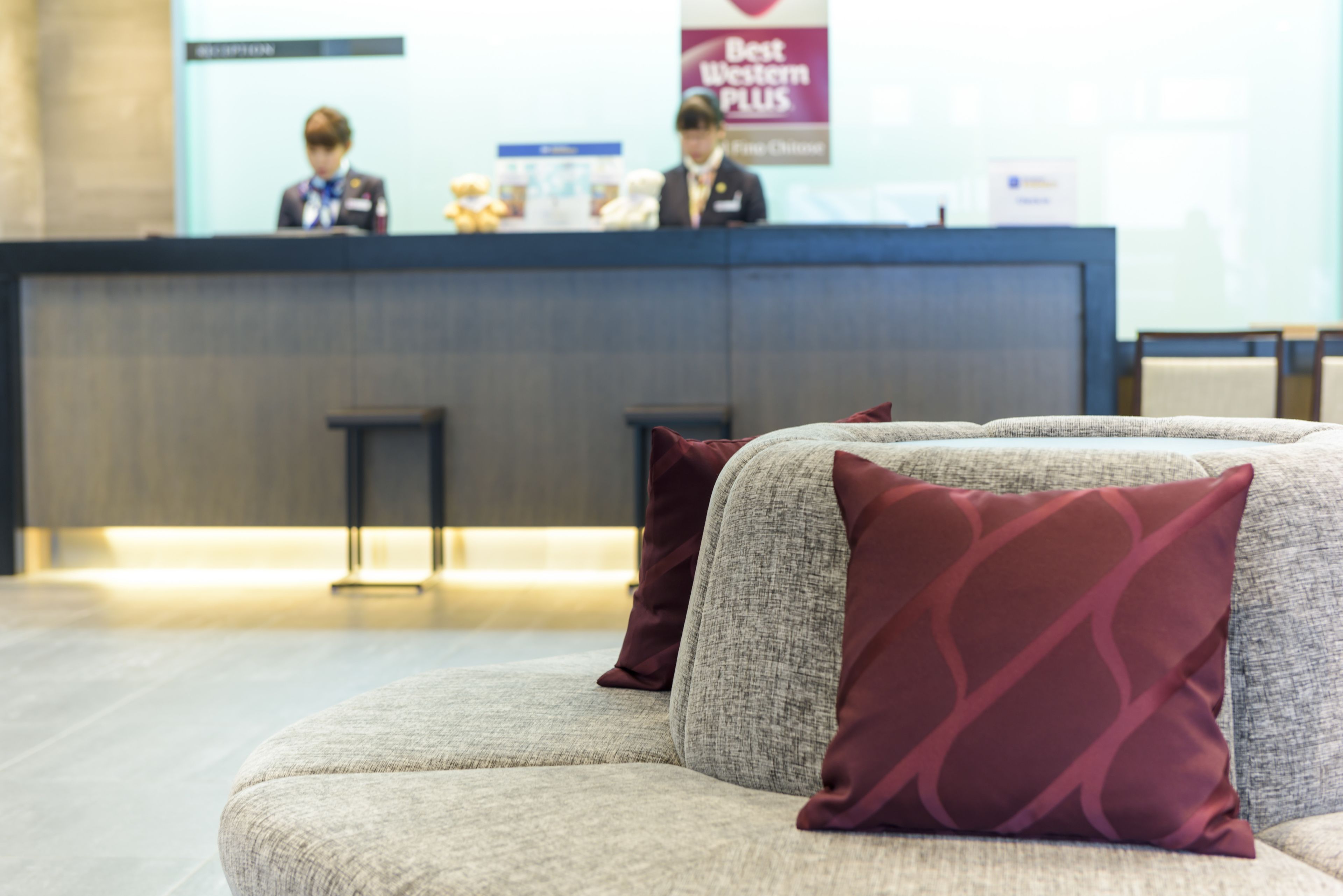 A hotel reception area with a counter, two bar stools, and a sofa with patterned cushions.