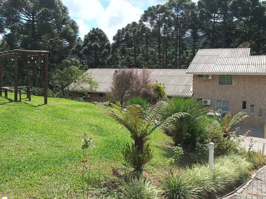 Un edificio con techo de tejas, un jardín con pérgola de madera y un sendero pavimentado.