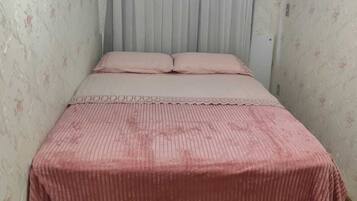A bedroom with a bed, a window with curtains, and an air conditioning unit.