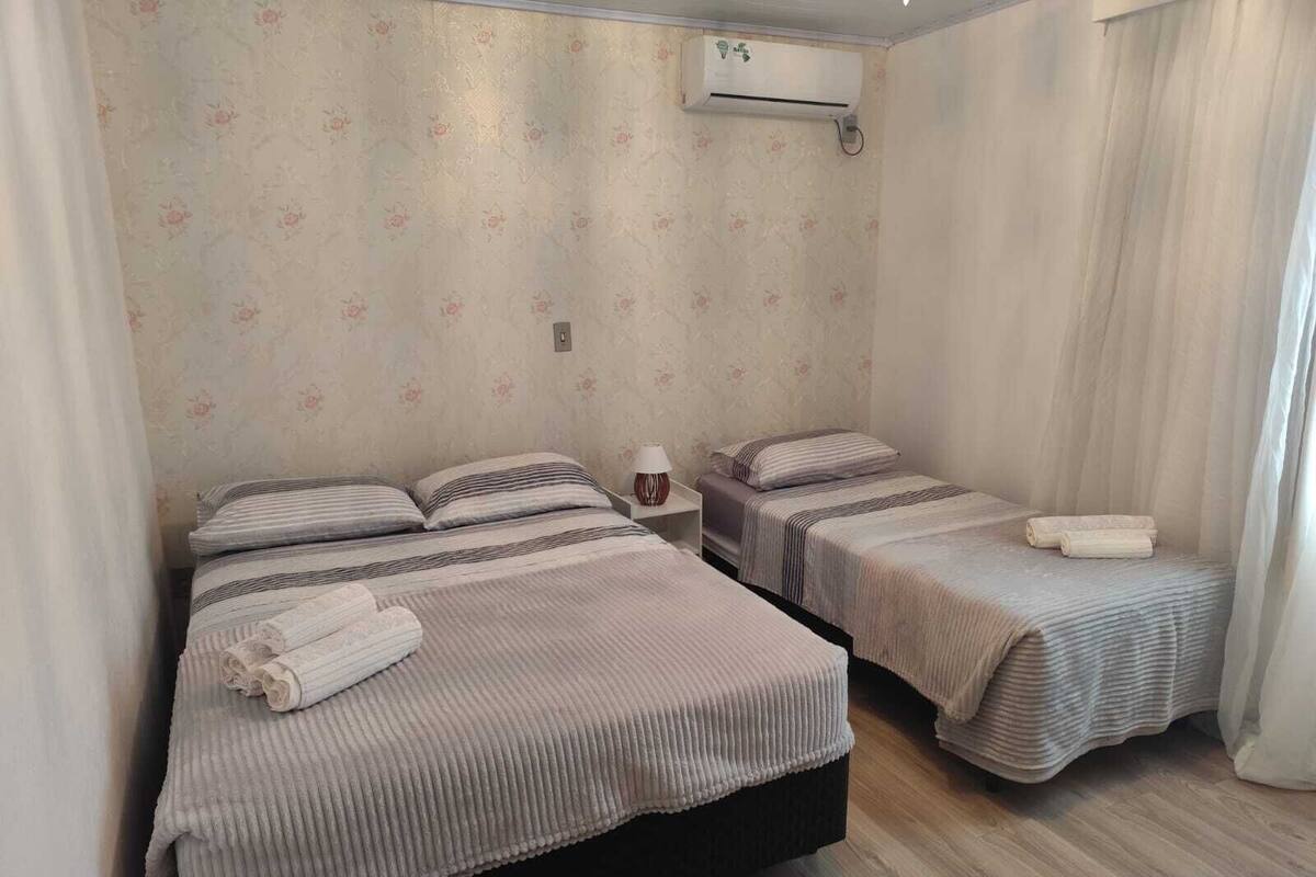 Habitación de hotel con dos camas, una mesita de noche, un equipo de aire acondicionado y papel tapiz con motivos florales.
